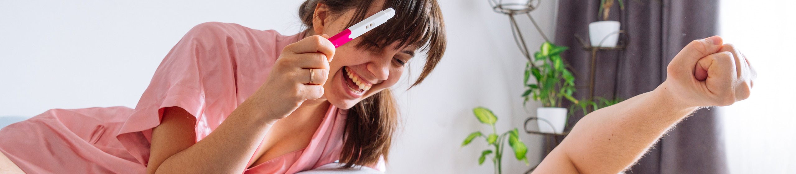 happy couple in bed. woman showing man positive pregnancy test.