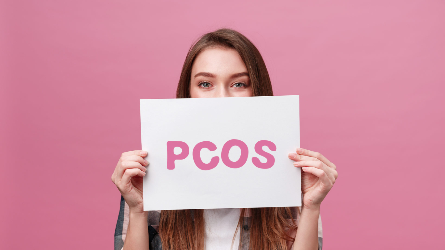 Ženska drži napis PCOS na rožnatem ozadju